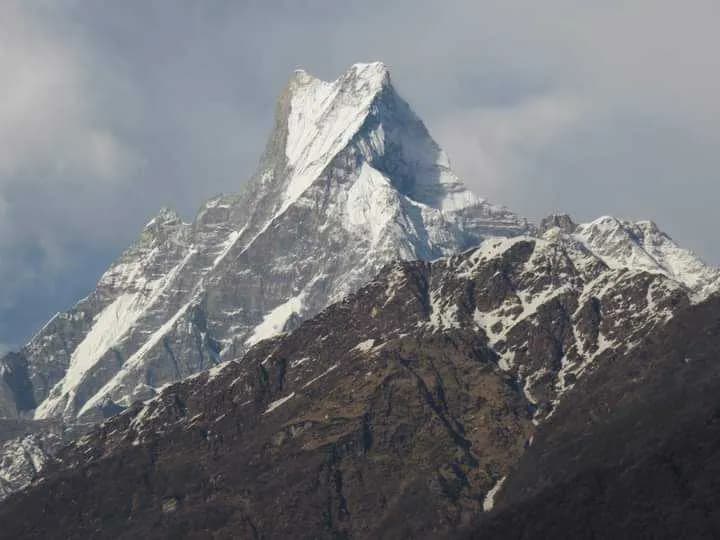 The iconic fishtail peak of Machhapuchhre standing tall against a cloudy sky during the ABC trek
