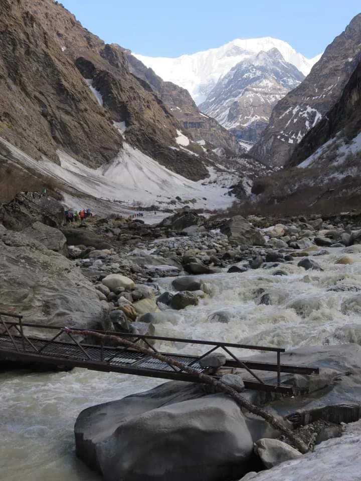 A trekking bridge over a fast-flowing glacial river in a deep valley on the way to Annapurna Base Camp