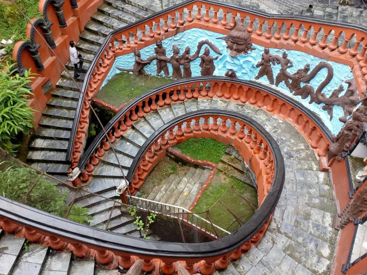 Ornate spiral staircase with Hindu relief sculptures leading into Gupteshwor Mahadev Cave
