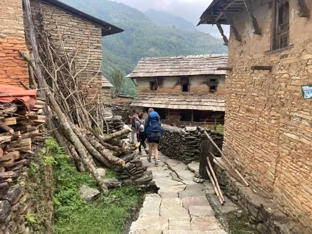 Trekkers walk through a traditional village of stone houses and slate roofs on the Panchase trail