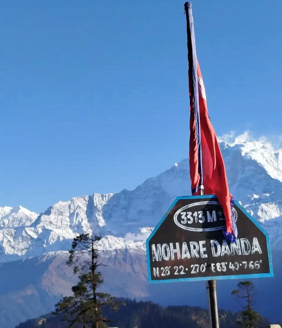 Mohare Danda 3313m summit sign and Nepal flag with snowy mountains in the background