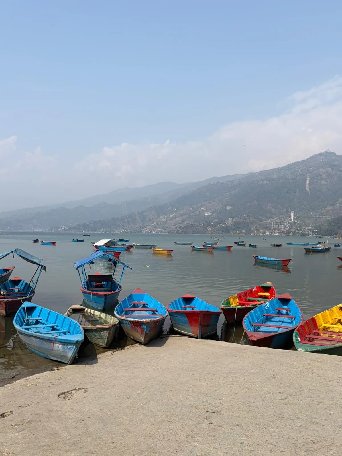 Brightly colored wooden boats docked at the shore of Phewa Lake against a backdrop of misty hills