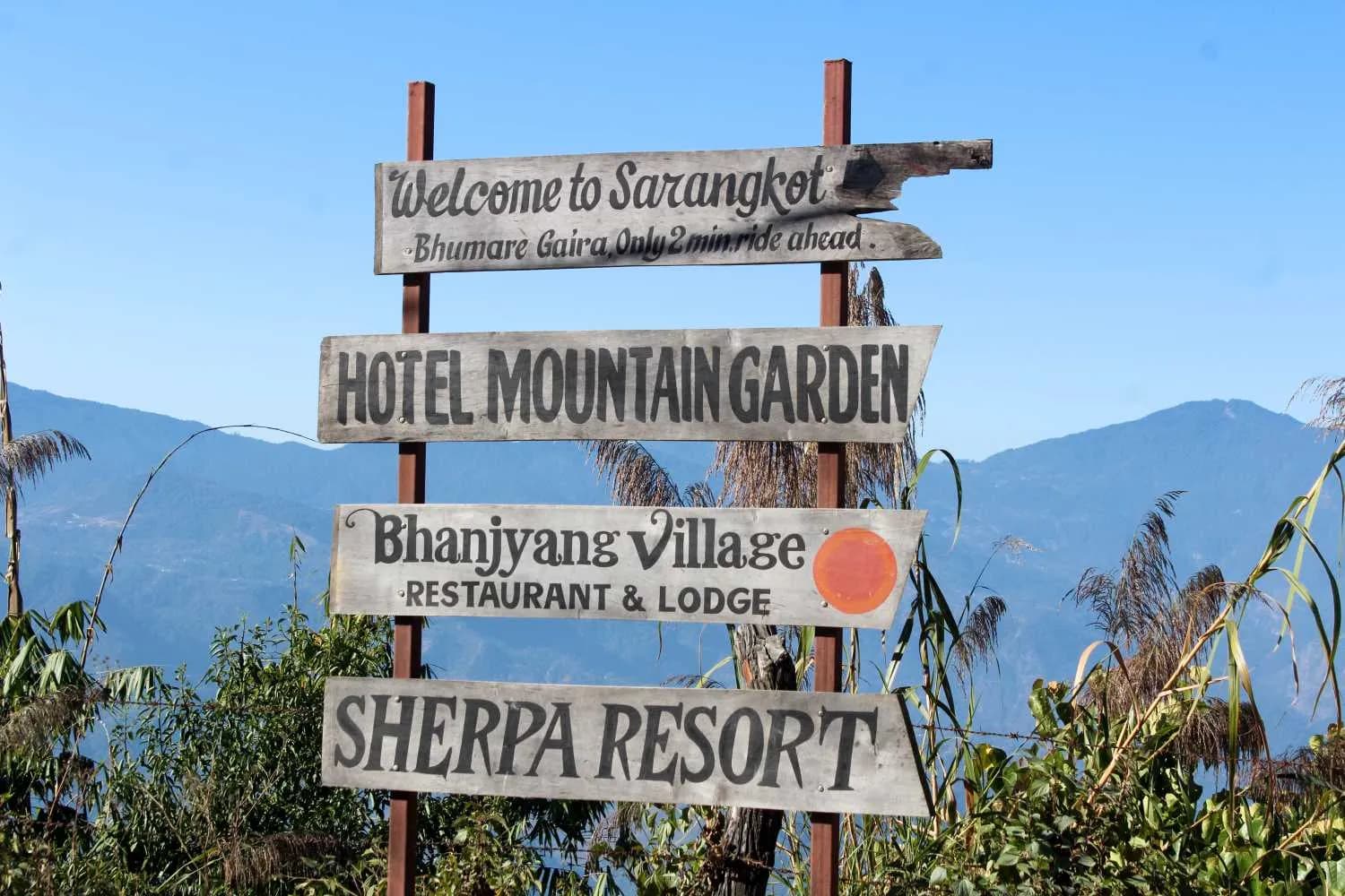 Wooden trail signs for Sarangkot and local lodges against a clear mountain backdrop