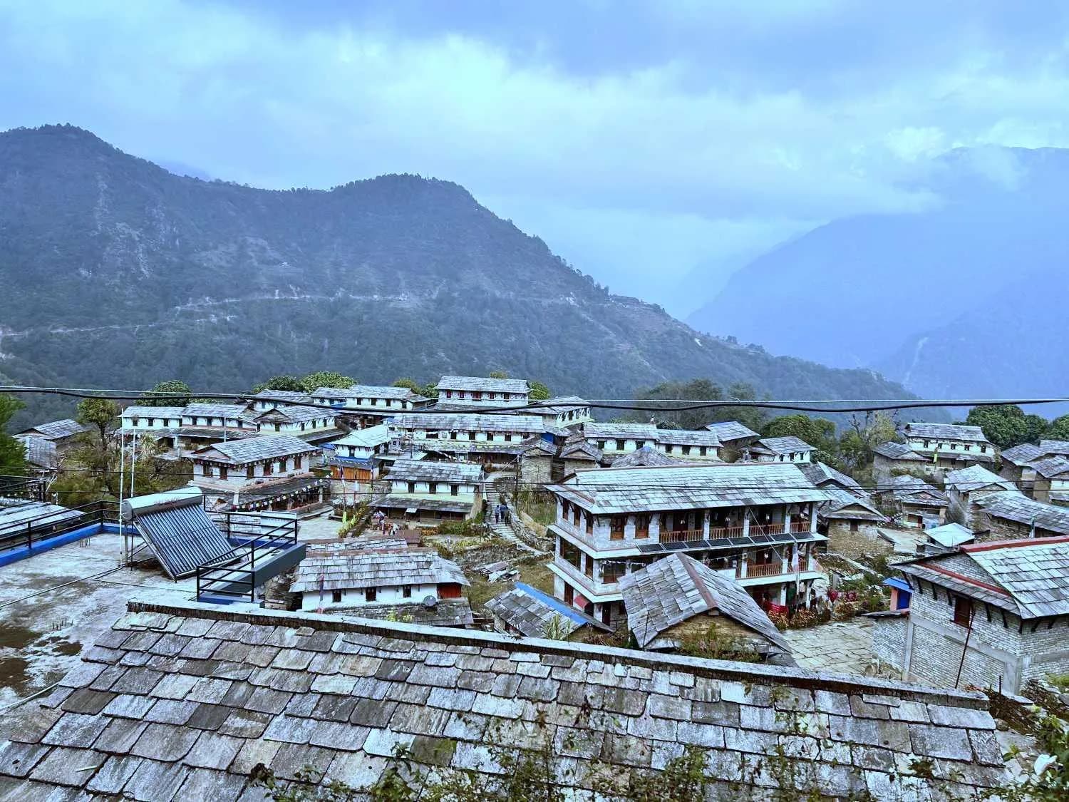 Ghandruk village with traditional slate-roofed houses under a cloudy sky and distant mountain ridges